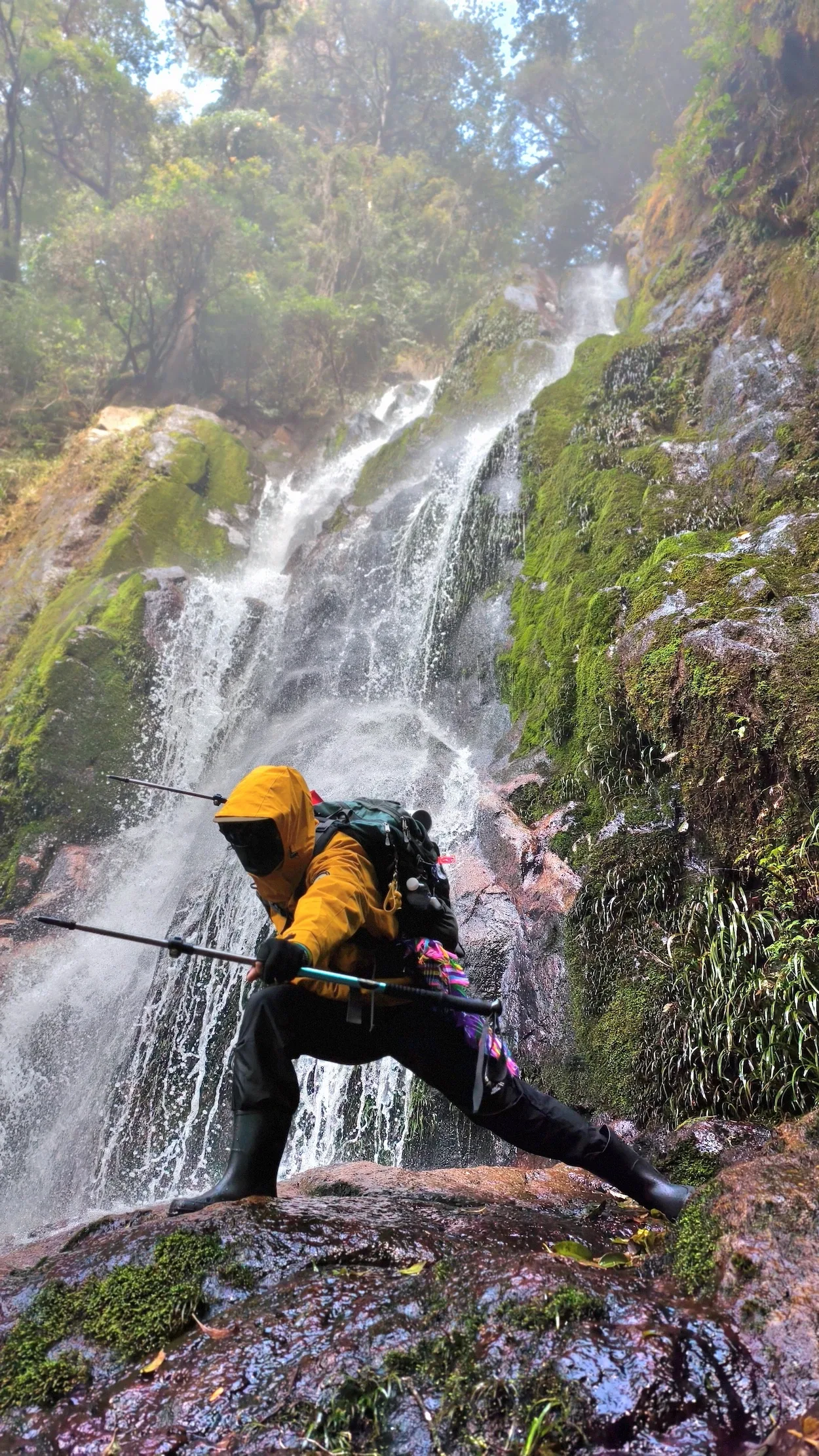 Người trekking áo cam đứng bên thác nước giữa rừng