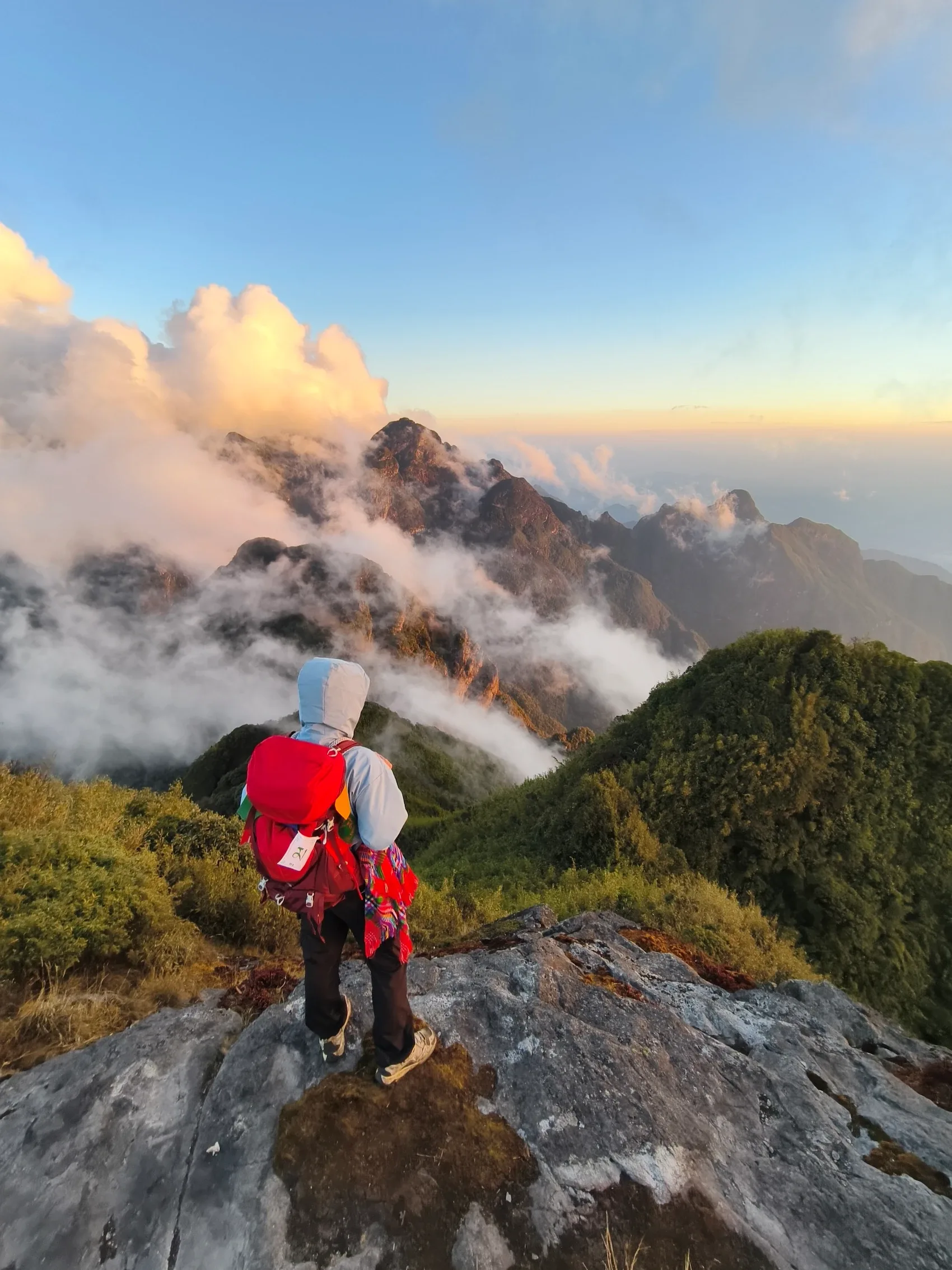Du khách đeo balo đỏ bước xuống sống núi đá giữa biển mây trên cung Miêu - Chu - Cán