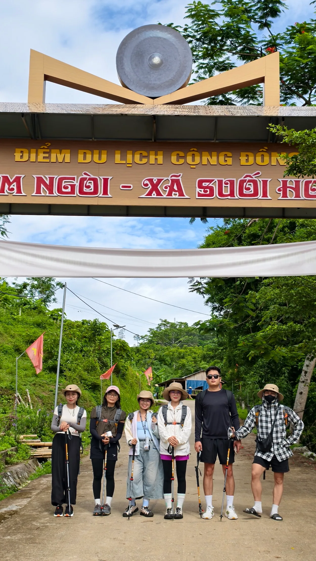 Đoàn du khách cầm gậy trekking chụp ảnh tại cổng Điểm du lịch cộng đồng Ngòi - Xã Suối Hoa