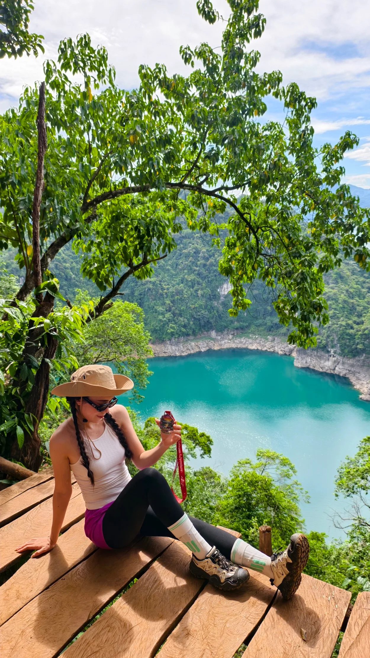 Nữ du khách ngồi trên sàn gỗ cầm huy chương, view hồ nước xanh ngọc phía dưới