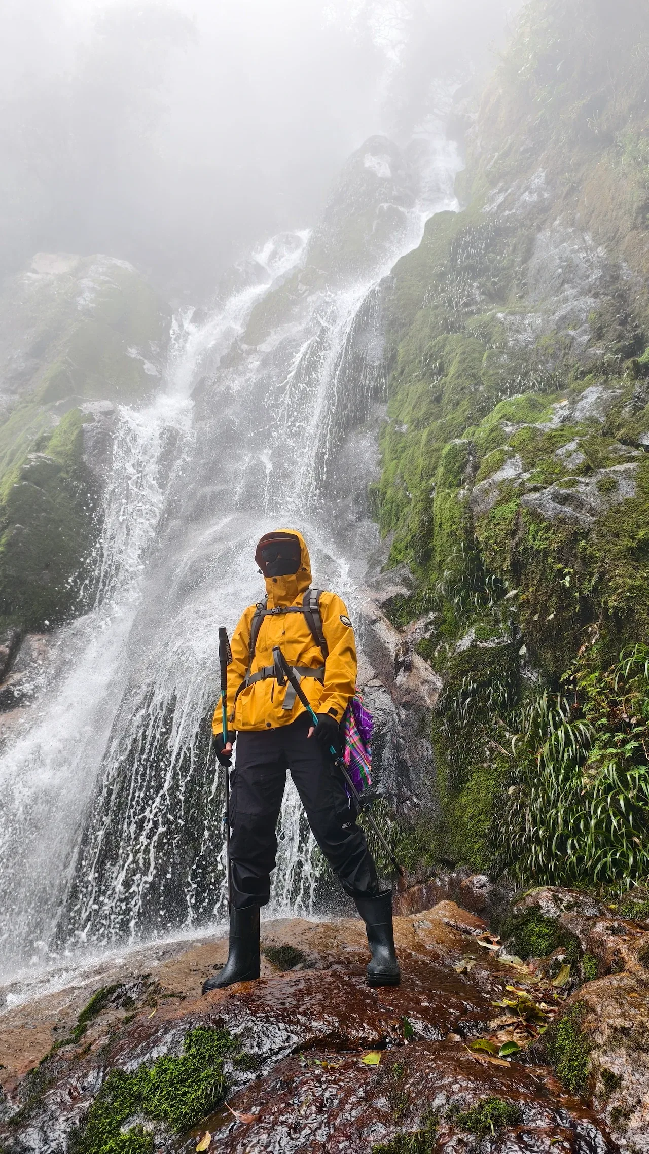 Người trekking đeo ba lô đứng trước dòng thác phủ sương