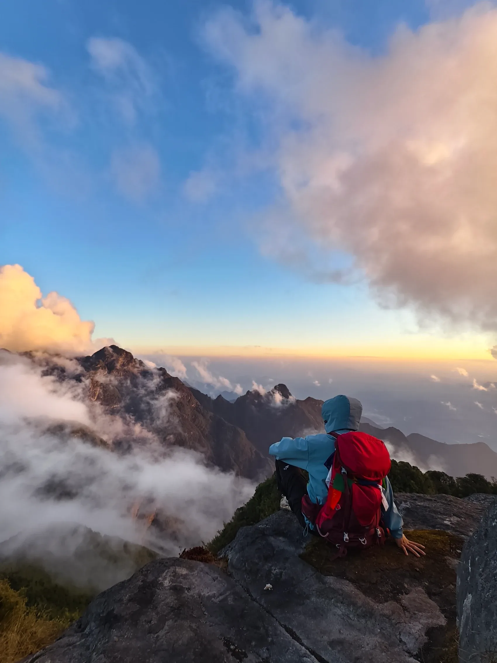 Du khách đeo balo đỏ ngồi nghỉ trên sống núi đá nhìn ra mây phủ Hoàng Liên Sơn