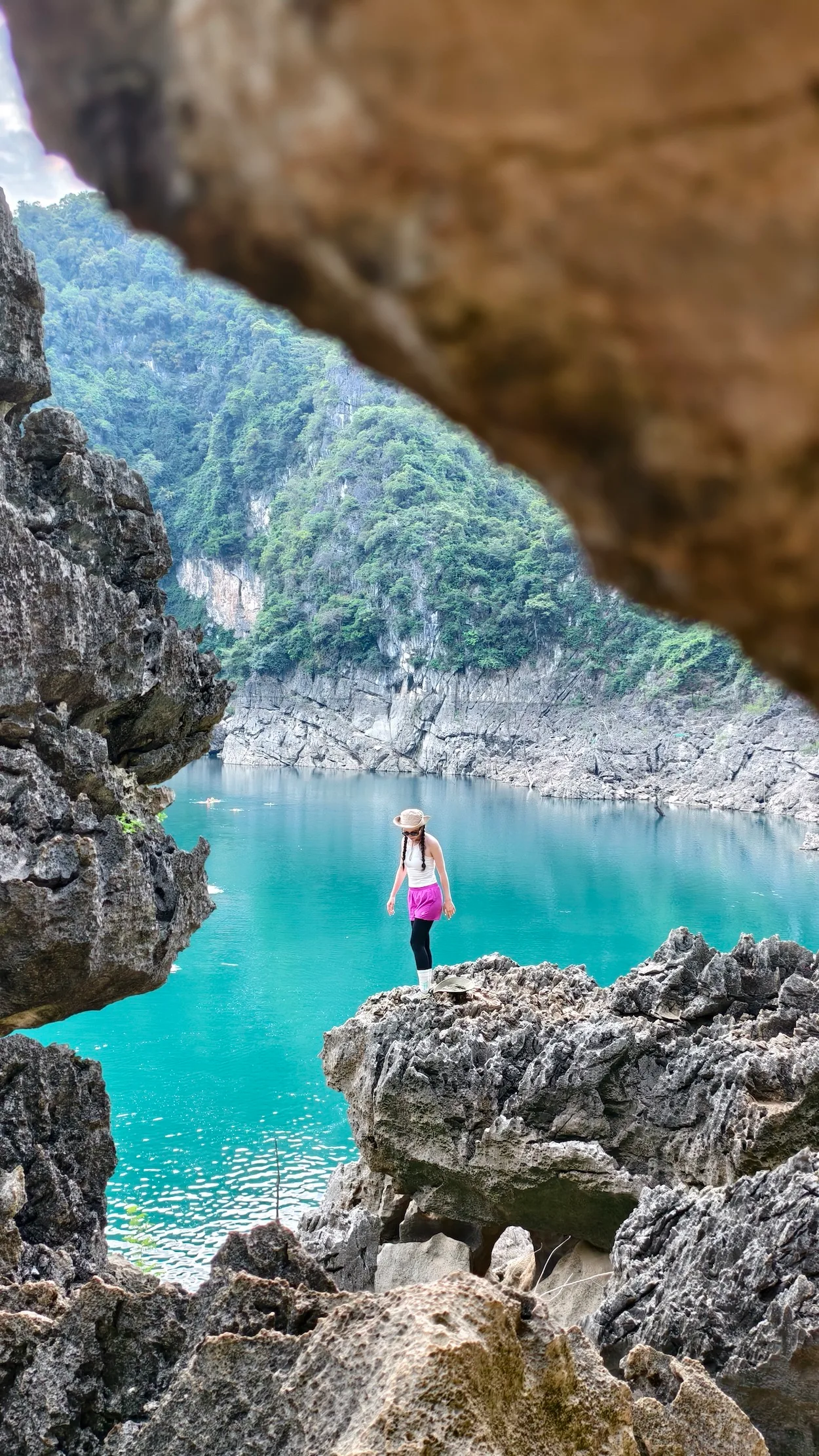 Nữ du khách đứng trên mỏm đá nhìn xuống hồ nước xanh ngọc, khung hình qua khe đá