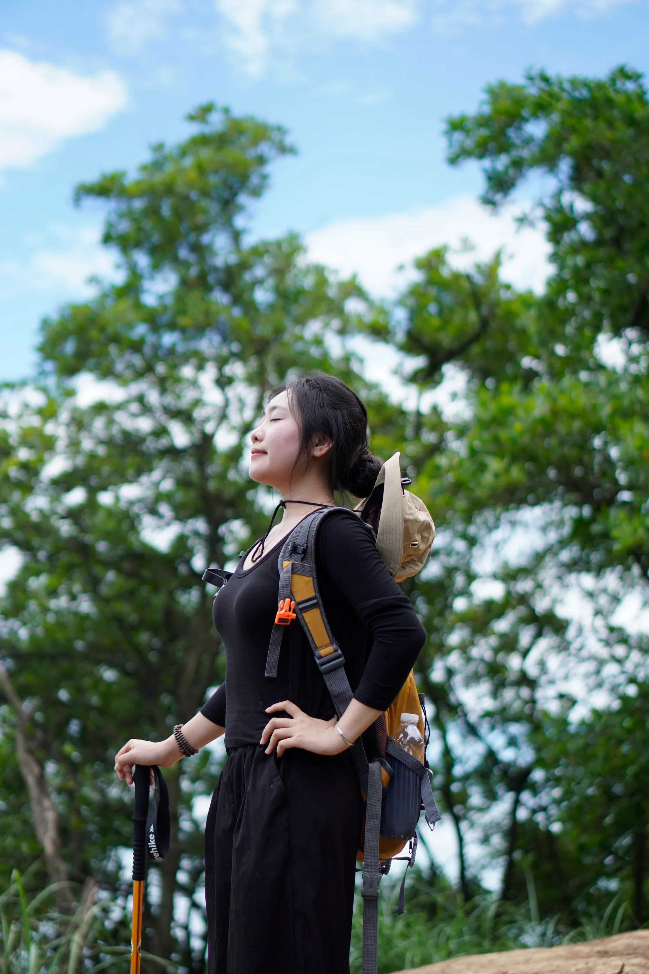 Nữ du khách đeo balo ngước nhìn tán cây trên đường trekking