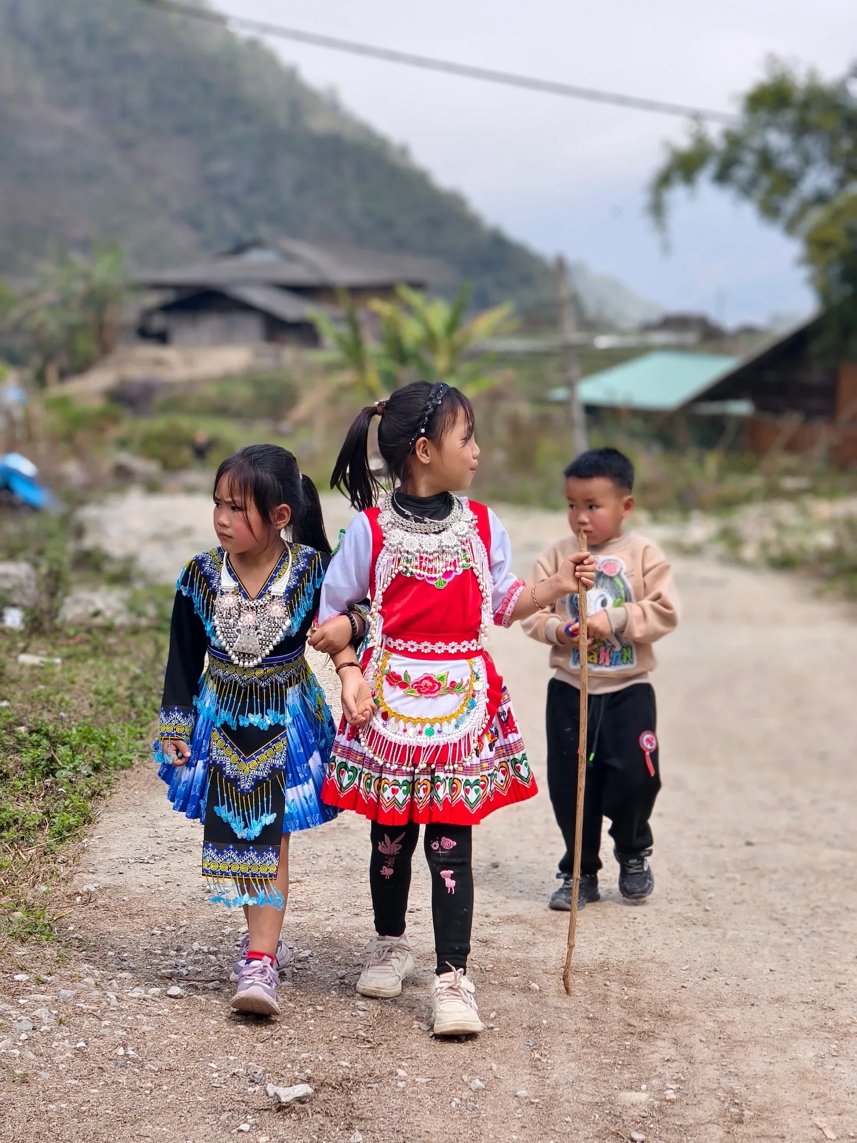 Các em nhỏ trong trang phục dân tộc đi trên đường bản