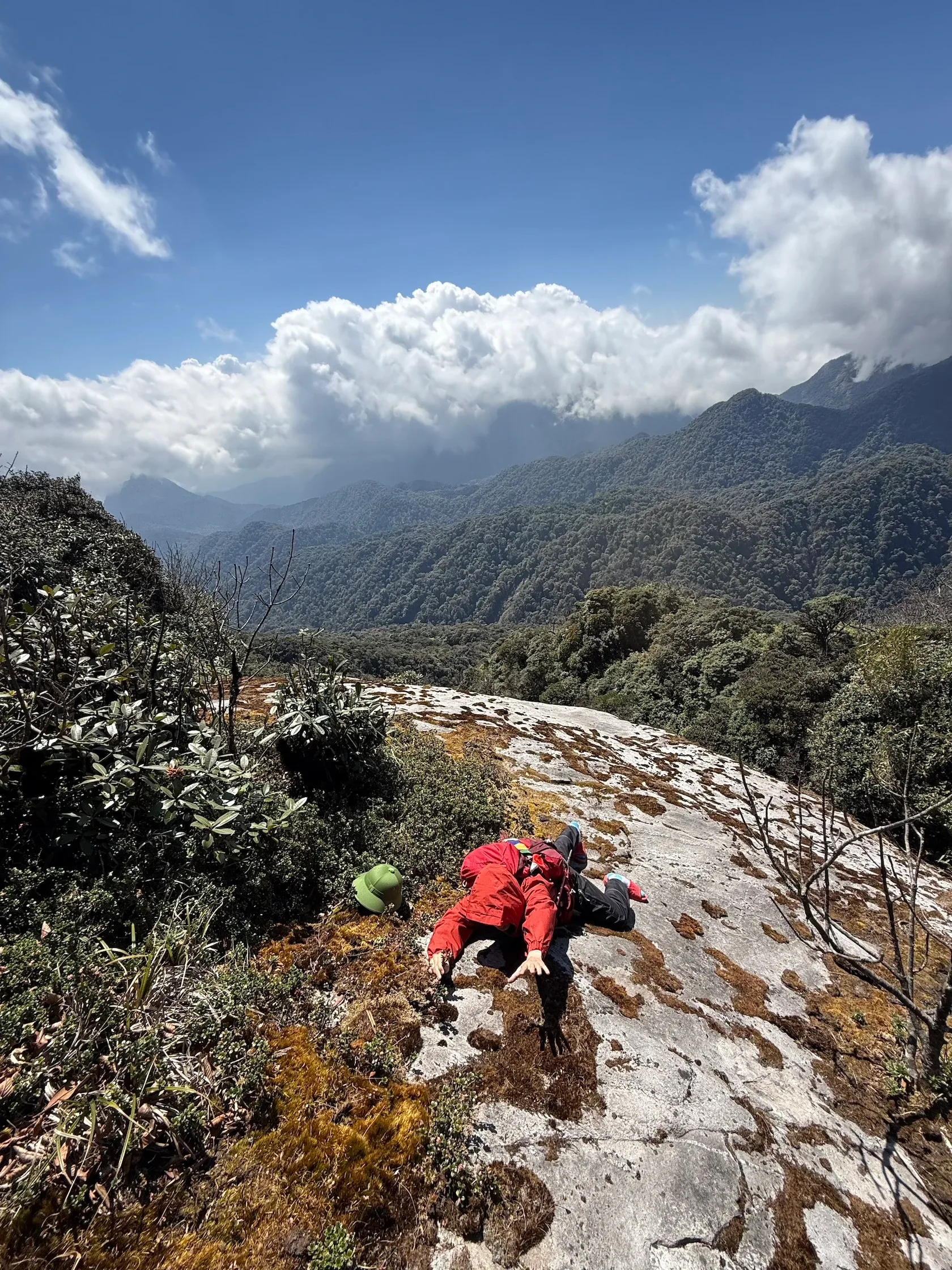 Đoàn trekking áo đỏ leo trên sườn đá dưới những đỉnh núi phủ mây
