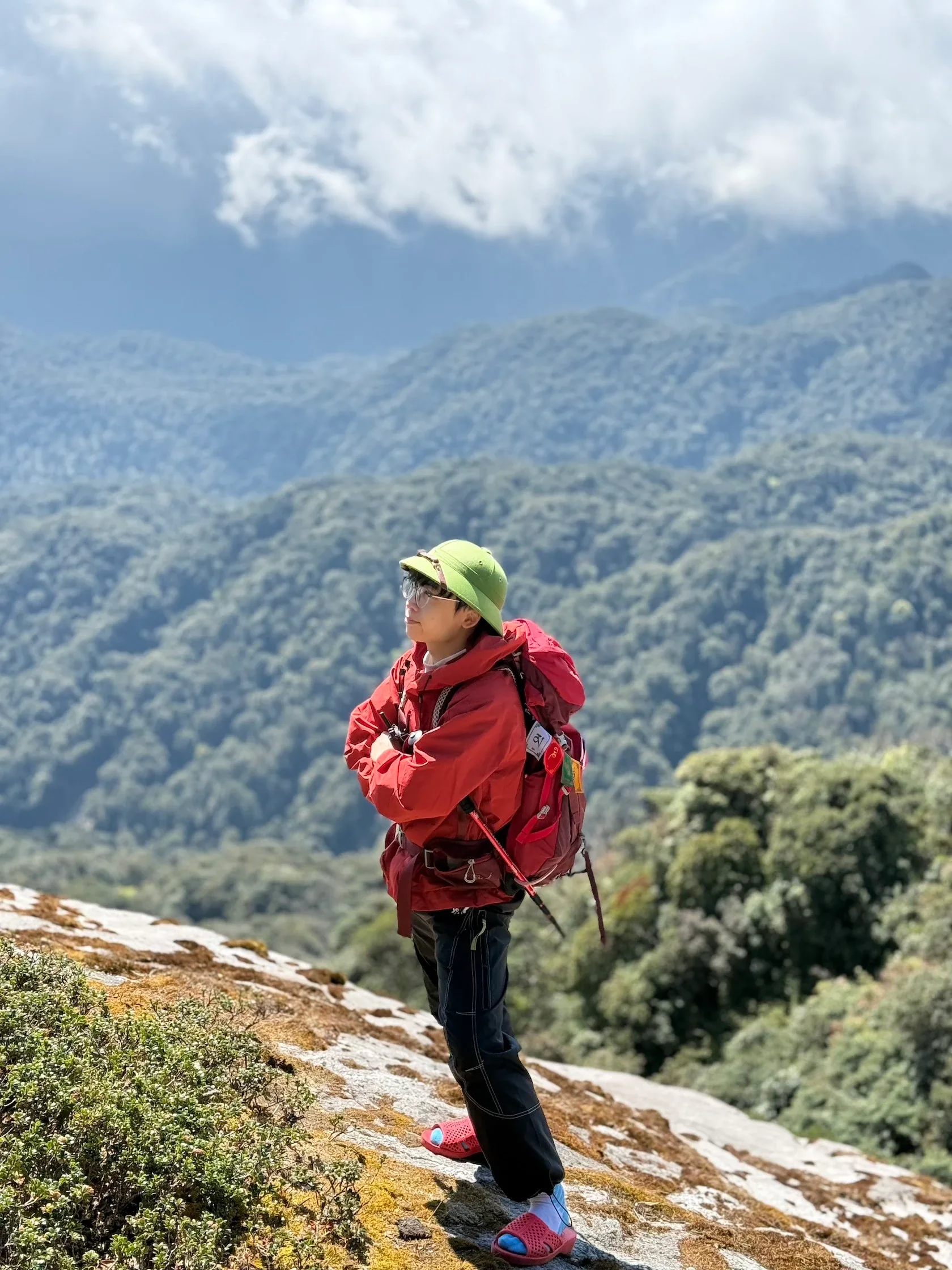 Nữ du khách áo đỏ đứng trên sườn đá nhìn xuống thung lũng xanh