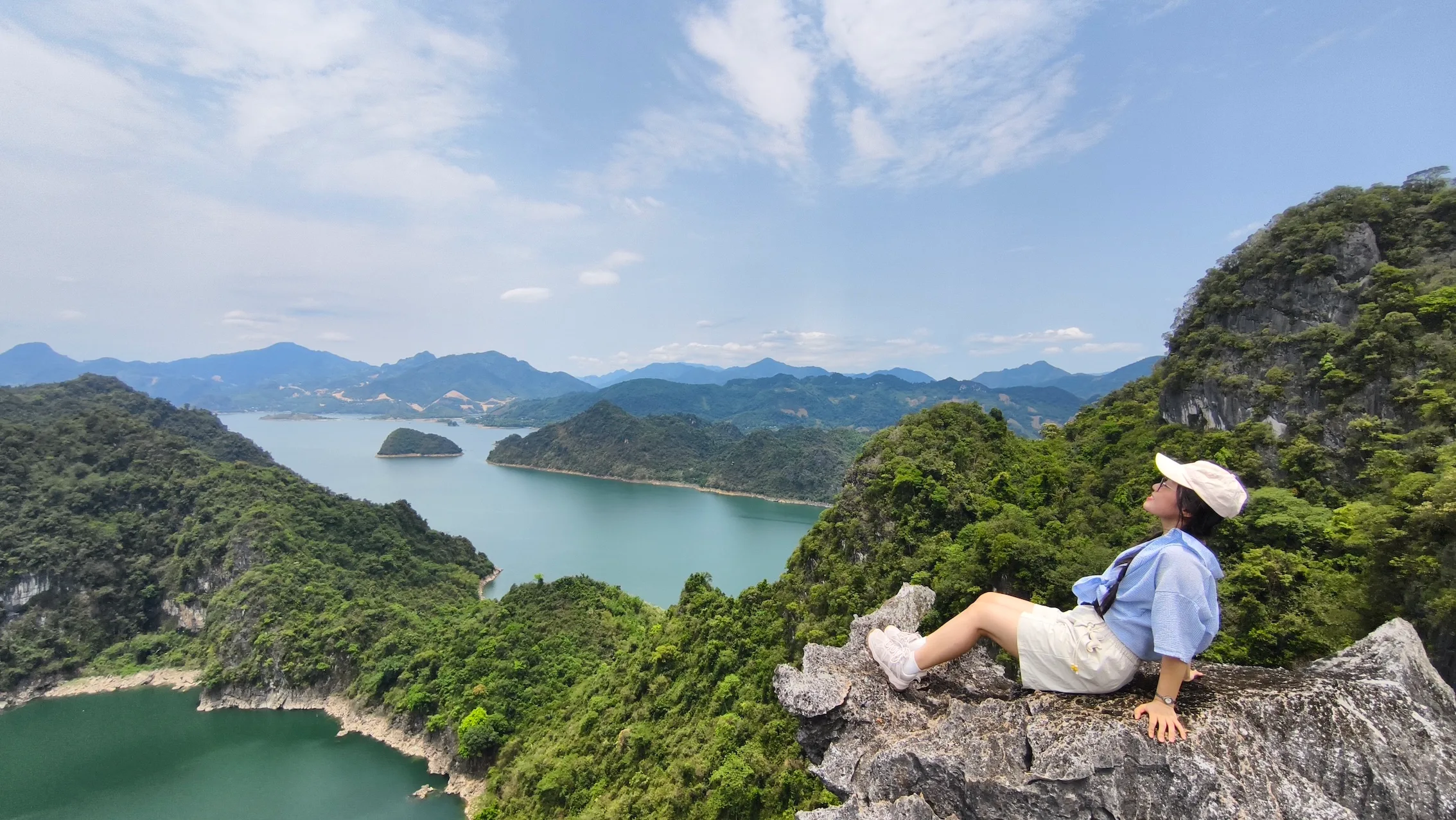 Nữ du khách tựa lưng trên mỏm đá cao, ngắm toàn cảnh hồ nước và các đảo nhỏ giữa lòng hồ