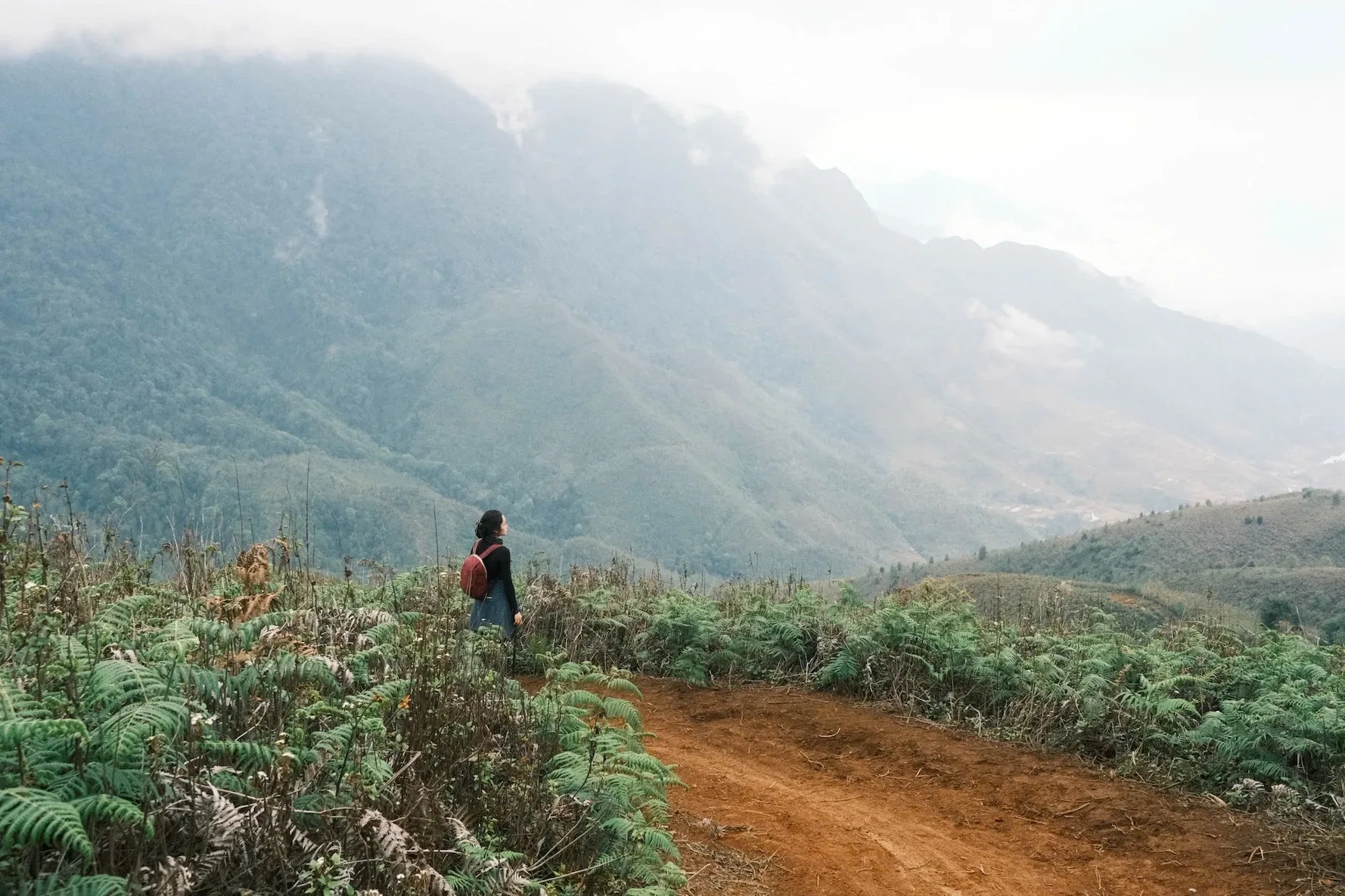 Người trekking đi trên con đường đất nhìn xuống núi rừng phủ sương